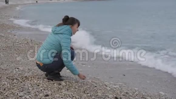 孤独寒冷海滩的女人可爱的白种人女人在海滩上水边玩石头视频的预览图