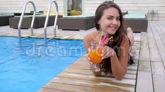年轻女子穿着泳衣手里拿着鸡尾酒在泳池边放松视频的预览图