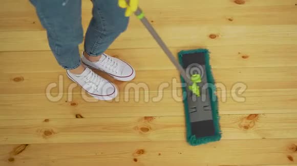 戴着防护手套的漂亮年轻女子在家里擦地板时用平的湿拖把的剪短图像视频的预览图
