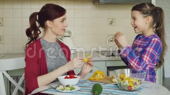 快乐的一家年轻的母亲和可爱的女儿在厨房做饭的时候玩着鬼脸用蔬菜傻乎乎的视频的预览图