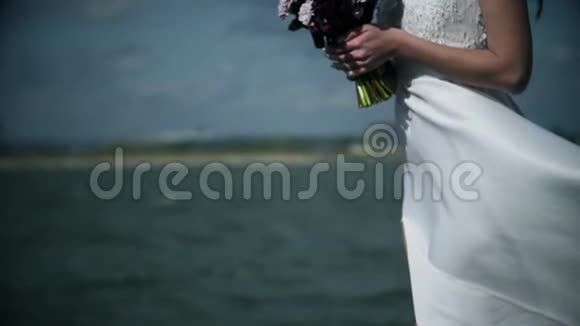 可爱的黑发女孩穿着白色连衣裙站在海洋上手里拿着一束花视频的预览图