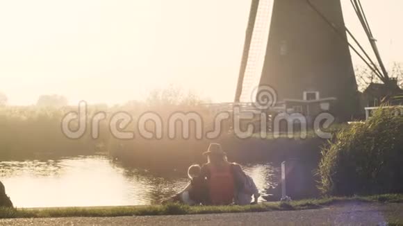 日落时分母亲带着两个孩子在小湖附近在码头上看到高加索家庭的宁静景象4K后视图视频的预览图