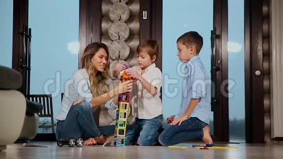 快乐的母亲带着两个孩子坐在乡间别墅的地板上花时间一起收集孩子视频的预览图