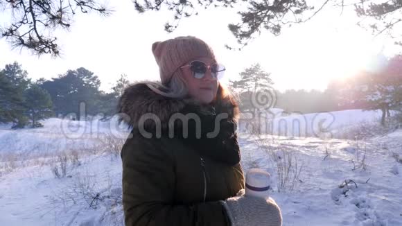 戴墨镜的可爱女孩在雪地森林里在冬天的户外用热饮料盛杯视频的预览图