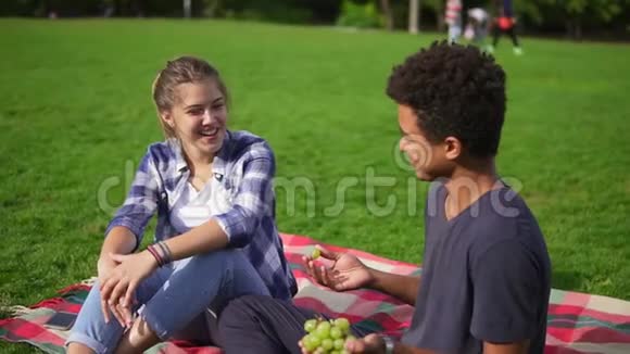 可爱的朋友坐在草地上夏天在公园里聊天帅哥手里拿着多汁的葡萄视频的预览图