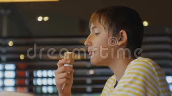 青少年吃快餐在快餐店吃冰淇淋锥的青少年男孩的特写镜头视频的预览图