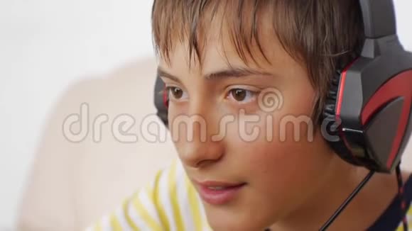 使用笔记本电脑的青少年青少年男孩在玩网络游戏时用耳机语音聊天的特写视频的预览图