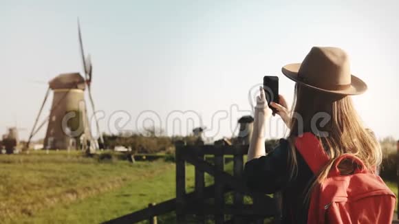 千禧旅游女孩合影风车旅行者女戴着红色背包享受田园风光4K视频的预览图
