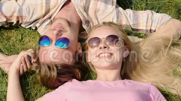 快乐的年轻夫妇享受周末躺在草坪上聊天夏天视频的预览图