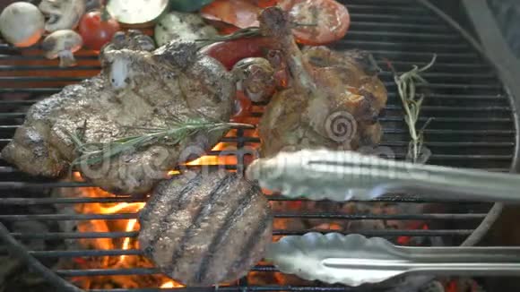 用迷迭香的枝条将肉串起来在背景烤蔬菜中厨师用钳子夹着肉视频的预览图