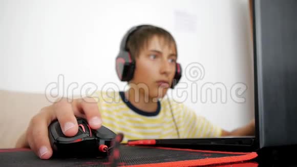 使用笔记本电脑的青少年带耳机的青少年使用有线鼠标在垫手动电脑游戏黑色和视频的预览图