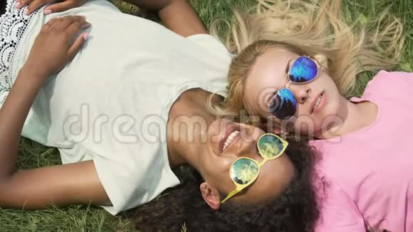 两个美丽的模特戴着太阳镜躺在草坪上摆姿势拍照夏天视频的预览图