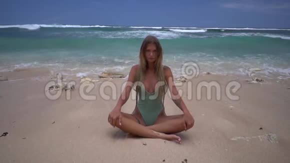 集中的年轻女子坐在莲花的位置在海浪中沙滩上有沙子美丽的放松和视频的预览图