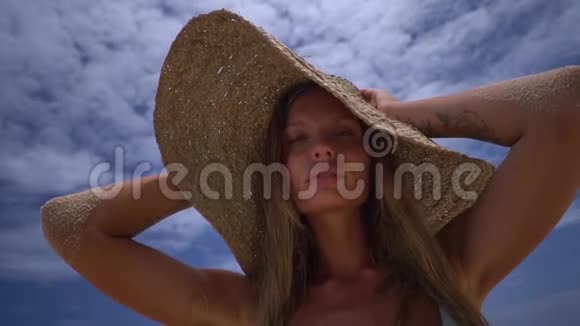 在沙滩上用草帽拍摄迷人女孩的肖像双手保留帽子这是一个美妙的假期视频的预览图