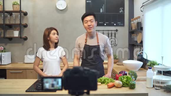 年轻的亚洲夫妇在厨房里用摄像机录制视频微笑的亚洲夫妇在写食物博客视频的预览图
