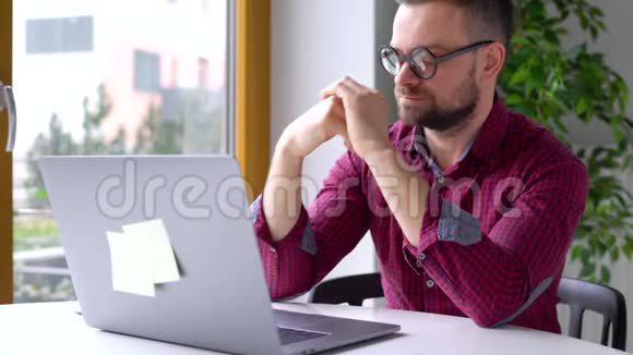 戴眼镜的大胡子男人坐在家里的办公室里用笔记本电脑工作视频的预览图