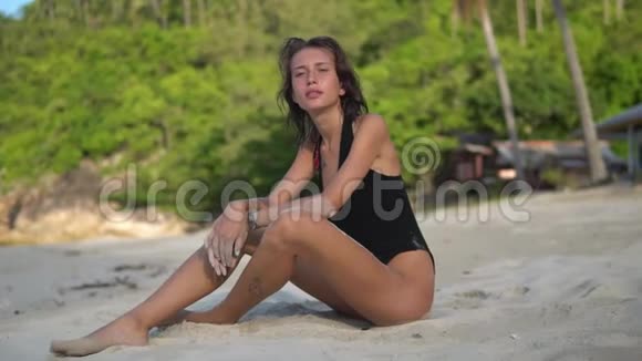 在热带森林的背景下一位身穿黑色比基尼坐在沙滩上的快乐年轻女子特写视频视频的预览图