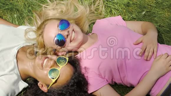两个美丽的女人躺在绿色的草坪上聊天在户外享受假期视频的预览图