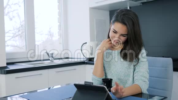 早上喝茶的时候可爱的女孩坐在网上用平板电脑视频的预览图