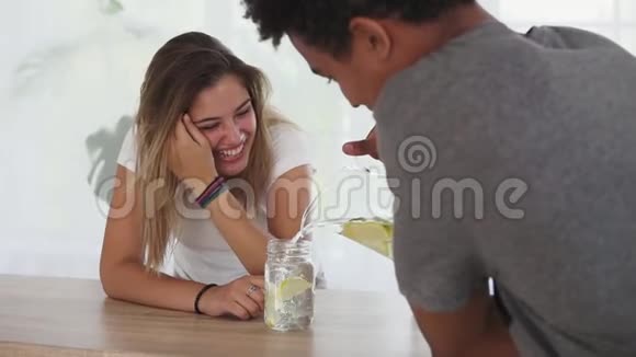 年轻的白种人女人端着一杯水坐在桌子旁和她的非洲男友交谈快乐的家庭享受视频的预览图