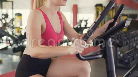 苗条的女人在体育俱乐部骑运动自行车健康的生活方式运动视频的预览图