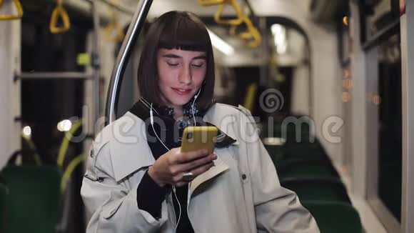 年轻时尚女性戴着耳机听音乐和在公共交通工具上浏览手机的肖像青年视频的预览图