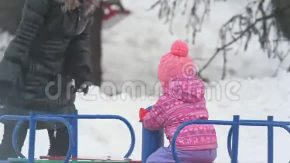 妈妈在冬天的旋转木马上围着她的小女儿转视频的预览图