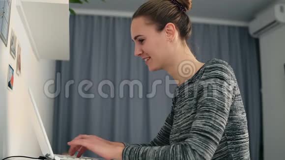 一位年轻女士坐在桌子旁手提电脑和打字快速地看着屏幕和屏幕视频的预览图