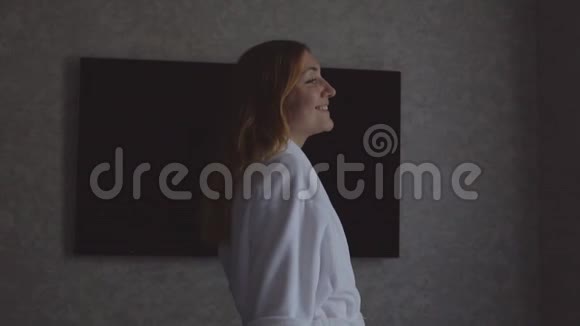 清晨穿着白色长袍的年轻快乐女孩望着窗外拉开窗帘视频的预览图