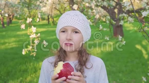 小女孩肖像吃红苹果户外花圃背景上有苹果的女孩视频的预览图