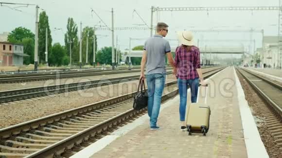一对带包的年轻夫妇在车站的站台上新婚夫妇去度蜜月背面视频的预览图