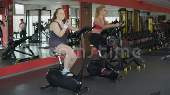 懒洋洋的胖女人在健身房里吃面包骑自行车视频的预览图