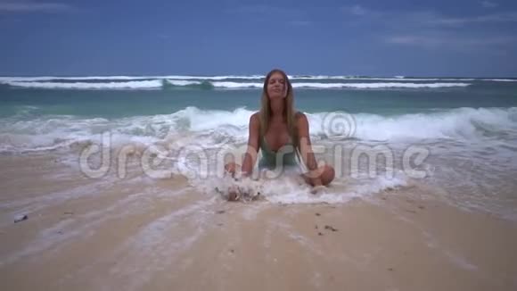 快乐的金发女人坐在莲花的位置在海浪中海滩上有粉红色的沙子美丽的放松和美丽的放松视频的预览图