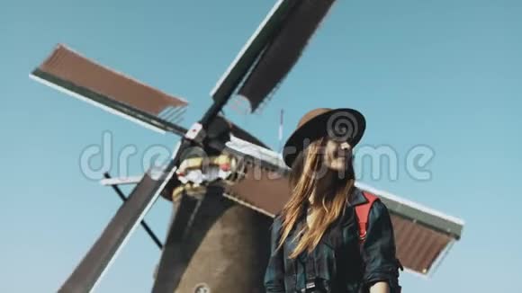 旧风车附近的女旅行者肖像不可思议的电影低角度在农场磨坊前戴帽子的女孩4K视频的预览图