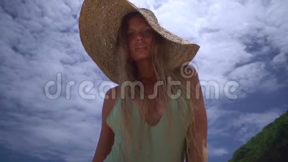 在海滩上一位身穿比基尼戴着时尚草帽的迷人年轻女子的肖像拍摄她看上去像在调情视频的预览图