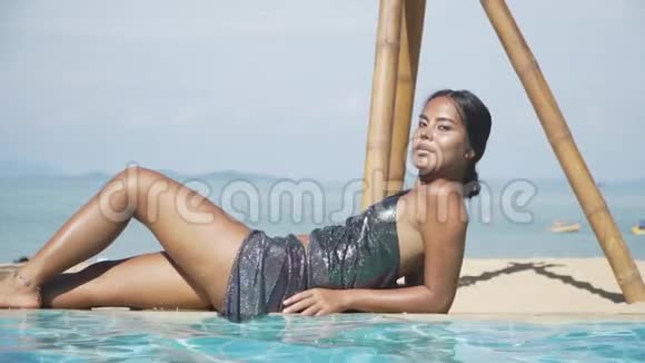 亚洲模特女孩躺在靠近水的池边一件闪亮的连衣裙上视频的预览图