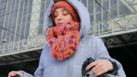 一位身穿蓝色外套头戴彩色帽子的年轻女子在晴朗寒冷的天气里在火车站拍摄的冬季肖像视频的预览图