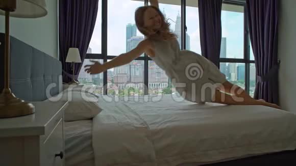 一个年轻女子在蜜月旅行中跳上床的慢镜头床垫和枕头概念视频的预览图