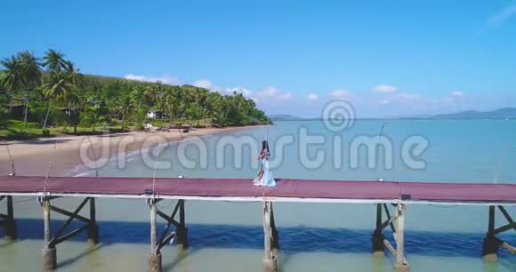 空中一个亚洲女孩走在码头上向海滩走去那里有棕榈树视频的预览图