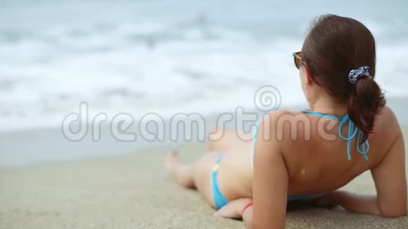 一个穿蓝色泳衣的女人躺在海滩上戴着太阳镜的布鲁内特躺在海里视频的预览图