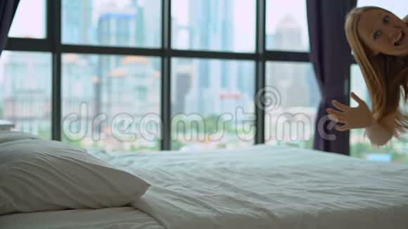 一个年轻女子在蜜月旅行中跳上床的慢镜头床垫和枕头概念视频的预览图