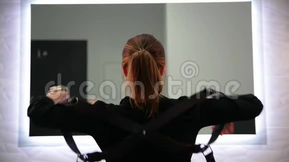 可爱的金发女人穿着黑色衬衫系着皮带站在浅灰色背景上看着镜子视频的预览图