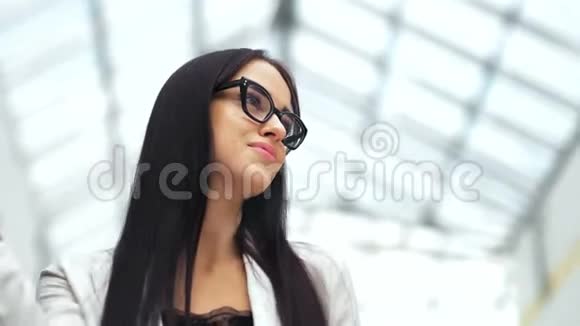 时尚的黑发模特拎着包看着相机在现代轻商场购物后微笑视频的预览图