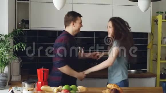 快乐又迷人的年轻一对恋爱中的情侣在度假时一起在厨房里跳舞视频的预览图