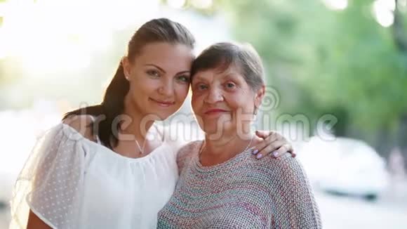 美丽的肖像祖母和她的孙女站在户外的夏天街黄金时间太阳耀斑女孩视频的预览图