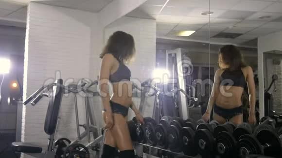 一个长着一头乌黑头发的漂亮运动的女孩站在大厅的镜子旁边看着她紧绷的身体转动视频的预览图