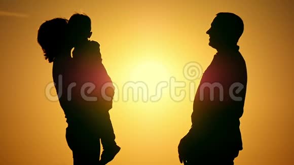 幸福家庭的剪影在日落的背景下慢动作拥抱妈妈把孩子抱在怀里爸爸拥抱着视频的预览图
