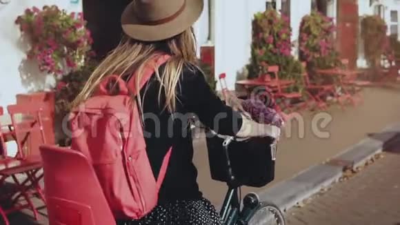 微笑的女孩骑着一辆带着红色背包的自行车慢动作特写欧洲女人带着鲜花沿着街道骑行视频的预览图