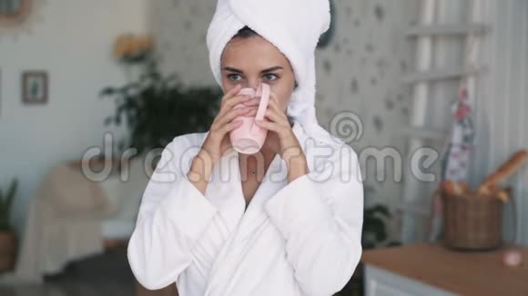 穿着浴袍的女孩肖像头上有毛巾喝咖啡或茶慢动作视频的预览图
