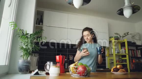 漂亮的快乐女孩在厨房里跳舞在智能手机上浏览社交媒体在家听音乐视频的预览图